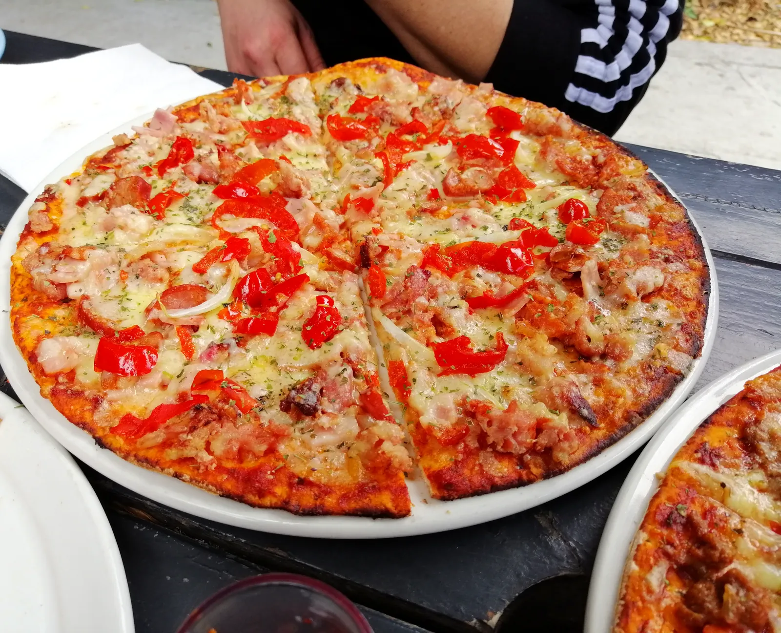 A Trenchtown pizza topped with red peppers and onion, sliced on a white plate